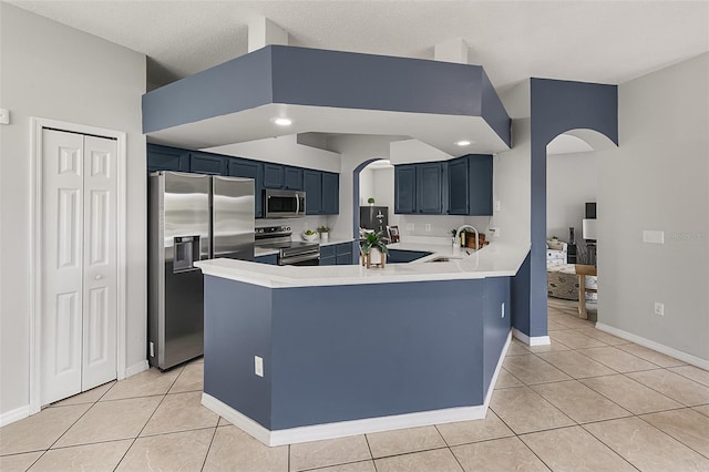 kitchen featuring a towering ceiling, blue cabinetry, sink, kitchen peninsula, and stainless steel appliances