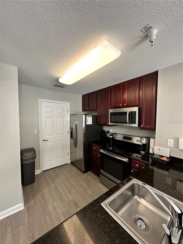 kitchen with appliances with stainless steel finishes, a textured ceiling, light hardwood / wood-style flooring, and sink