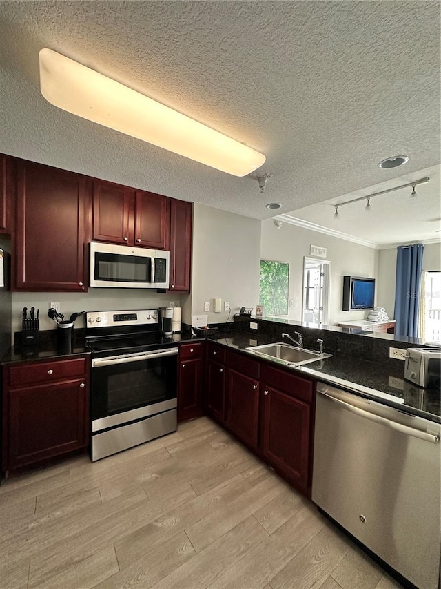 kitchen with appliances with stainless steel finishes, a textured ceiling, light hardwood / wood-style flooring, and sink