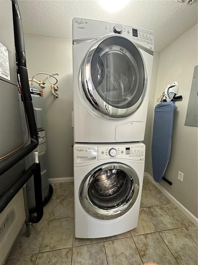 washroom featuring a textured ceiling, electric water heater, stacked washer and dryer, and light tile patterned flooring