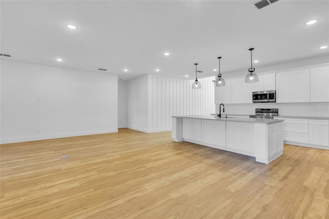 kitchen with white cabinetry, stainless steel appliances, decorative light fixtures, a center island with sink, and light wood-type flooring