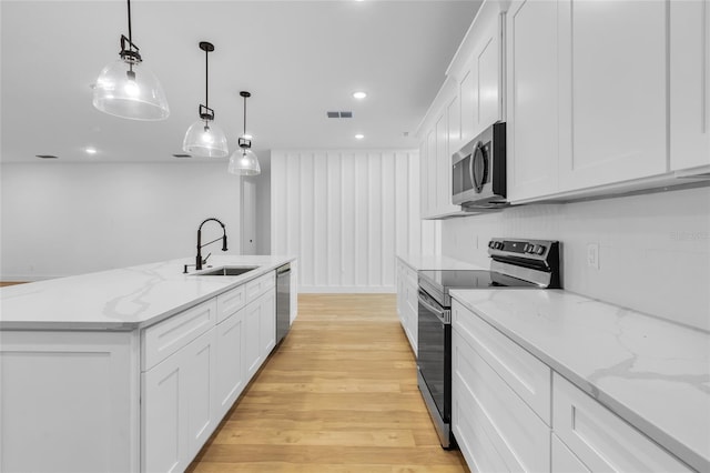 kitchen featuring a kitchen island with sink, hanging light fixtures, light hardwood / wood-style flooring, white cabinetry, and stainless steel appliances