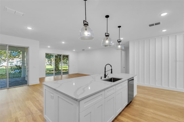 kitchen featuring sink, pendant lighting, a kitchen island with sink, white cabinets, and light wood-type flooring