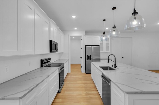 kitchen with stainless steel appliances, light hardwood / wood-style flooring, white cabinetry, hanging light fixtures, and an island with sink