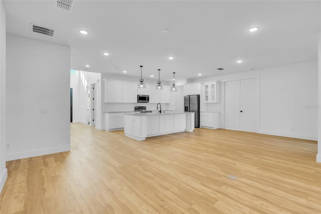 kitchen with pendant lighting, a kitchen island with sink, white cabinets, light hardwood / wood-style flooring, and appliances with stainless steel finishes