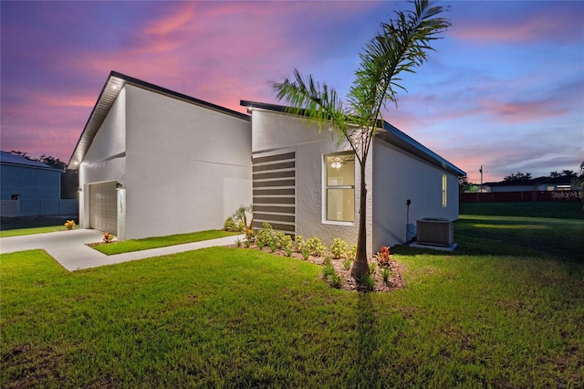 property exterior at dusk with a garage, a lawn, and cooling unit