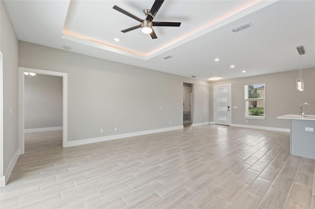 unfurnished living room featuring ceiling fan, a raised ceiling, and sink