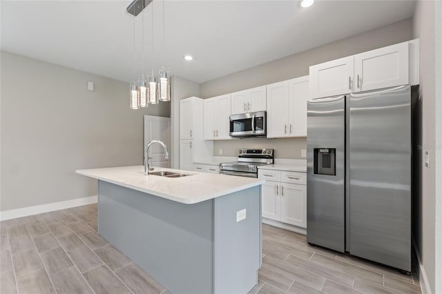 kitchen with white cabinets, hanging light fixtures, sink, an island with sink, and appliances with stainless steel finishes