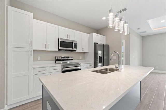 kitchen featuring light hardwood / wood-style floors, white cabinetry, appliances with stainless steel finishes, an island with sink, and pendant lighting