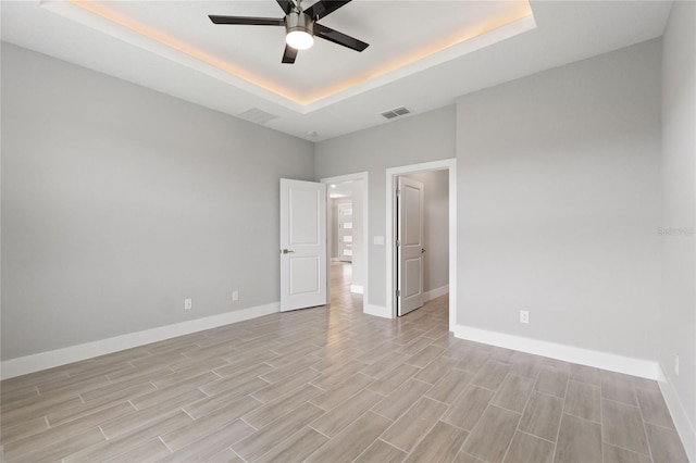 unfurnished room with light hardwood / wood-style floors, ceiling fan, and a raised ceiling