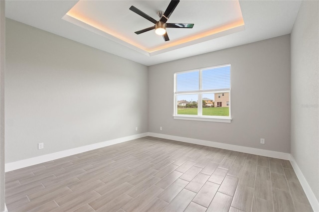 empty room with light hardwood / wood-style floors, ceiling fan, and a raised ceiling