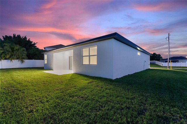 property exterior at dusk with a lawn and a patio