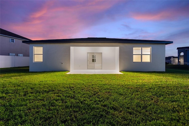 back house at dusk with a lawn and a patio