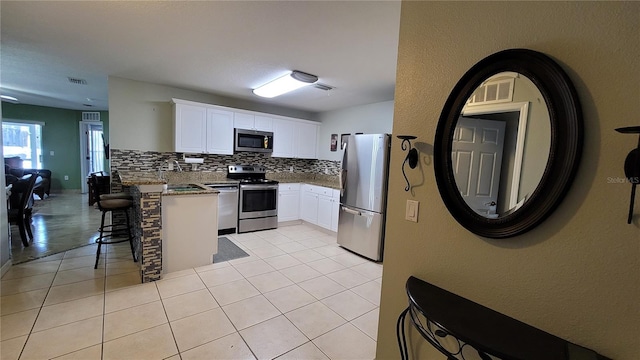 kitchen with stainless steel appliances, light tile patterned floors, tasteful backsplash, kitchen peninsula, and white cabinets