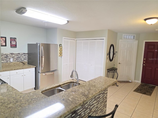 kitchen with decorative backsplash, light tile patterned flooring, stainless steel refrigerator, sink, and white cabinetry