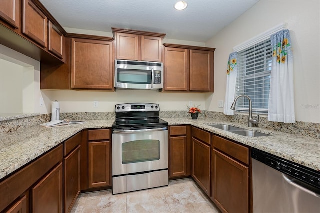 kitchen with sink, stainless steel appliances, a textured ceiling, and light stone countertops