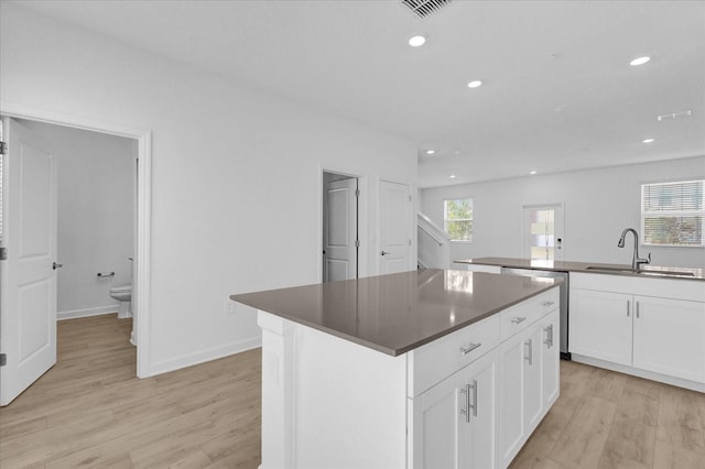 kitchen with a center island, sink, light hardwood / wood-style flooring, stainless steel dishwasher, and white cabinetry