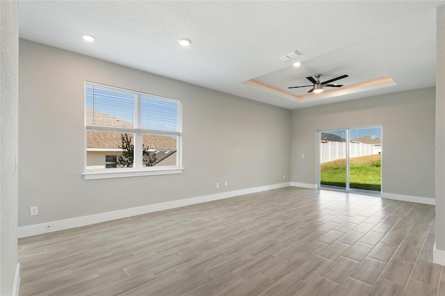 unfurnished room featuring a textured ceiling, light hardwood / wood-style floors, ceiling fan, and a tray ceiling