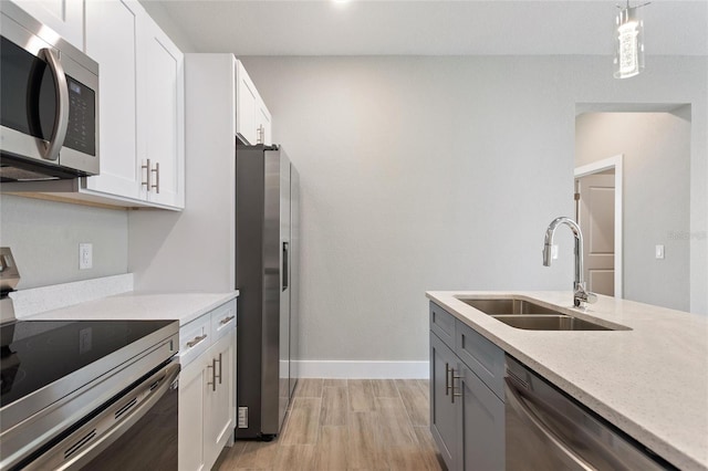 kitchen featuring light hardwood / wood-style floors, stainless steel appliances, sink, white cabinetry, and decorative light fixtures