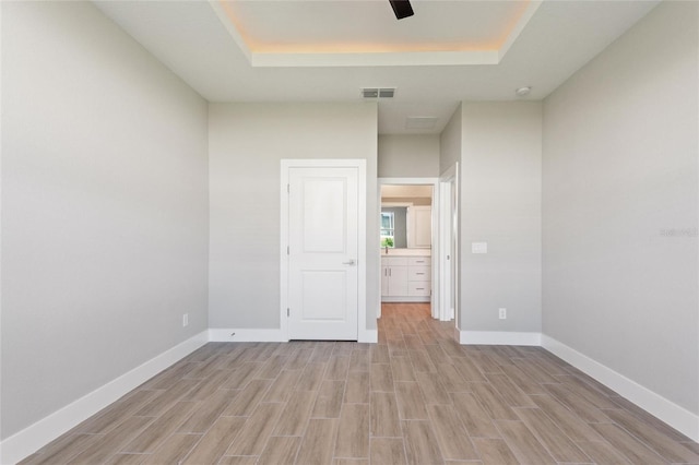 spare room with a tray ceiling and light hardwood / wood-style floors