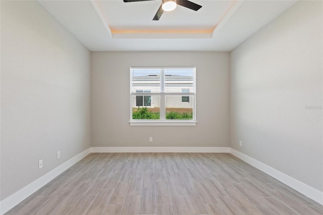 unfurnished room featuring light hardwood / wood-style floors, ceiling fan, and a raised ceiling