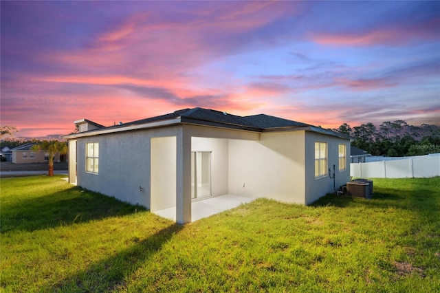 back house at dusk featuring central AC unit and a lawn