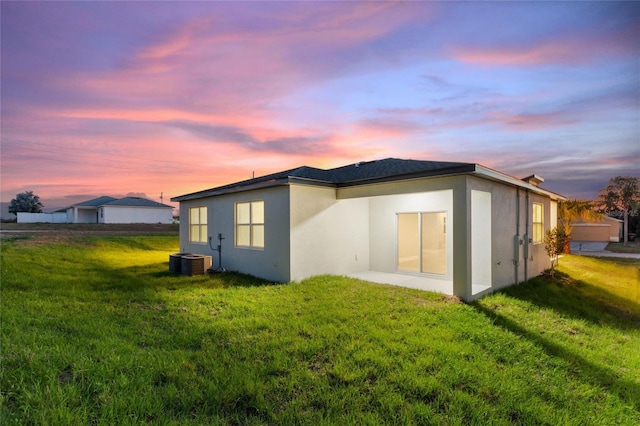 back house at dusk featuring central air condition unit and a yard