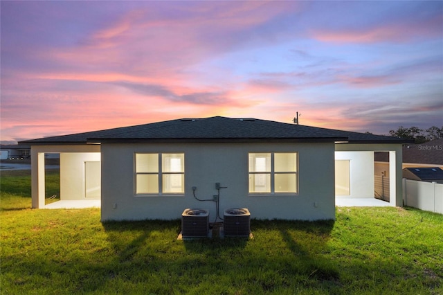 back house at dusk featuring central air condition unit, a yard, and a patio area