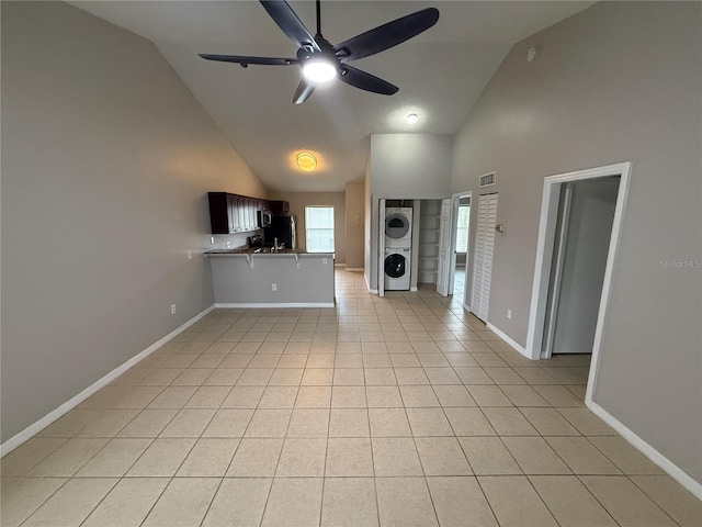 unfurnished living room with high vaulted ceiling, stacked washer and clothes dryer, light tile patterned floors, and ceiling fan