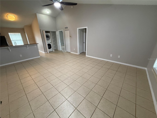 unfurnished living room with high vaulted ceiling, stacked washer / dryer, light tile patterned floors, and ceiling fan