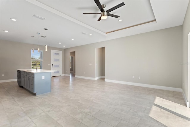 kitchen featuring a center island with sink, sink, ceiling fan, a raised ceiling, and decorative light fixtures