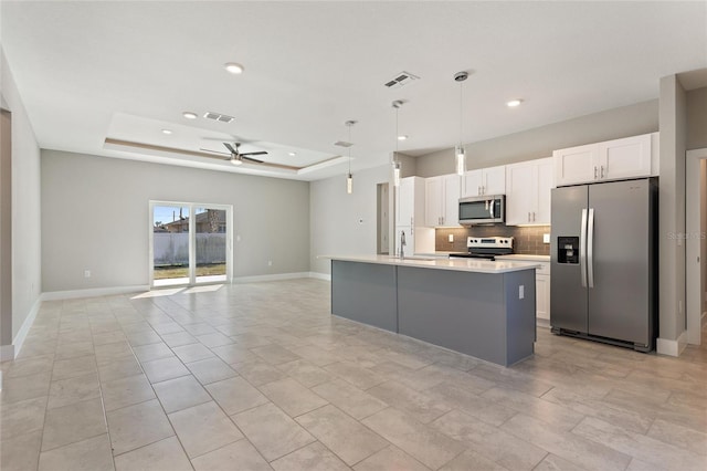 kitchen featuring stainless steel appliances, a center island with sink, a tray ceiling, white cabinetry, and decorative light fixtures