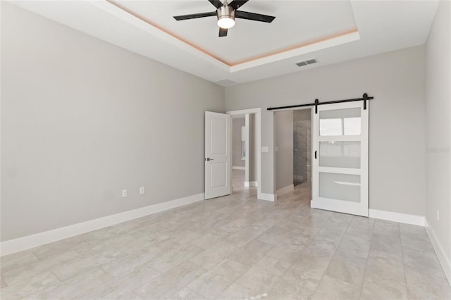 unfurnished bedroom featuring a barn door, ceiling fan, and a tray ceiling