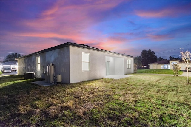 property exterior at dusk with central AC unit and a lawn