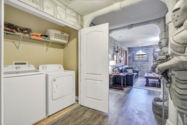 clothes washing area featuring washing machine and clothes dryer, a textured ceiling, and hardwood / wood-style flooring