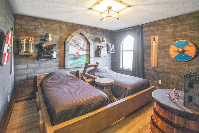 bedroom with brick wall, a textured ceiling, and hardwood / wood-style flooring