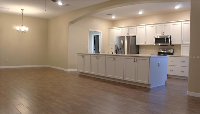 kitchen featuring appliances with stainless steel finishes, white cabinetry, dark hardwood / wood-style flooring, hanging light fixtures, and a center island with sink