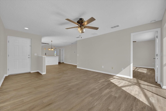 unfurnished living room featuring ceiling fan with notable chandelier, a textured ceiling, and light wood-type flooring