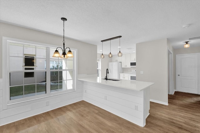 kitchen with sink, decorative light fixtures, kitchen peninsula, white appliances, and white cabinets