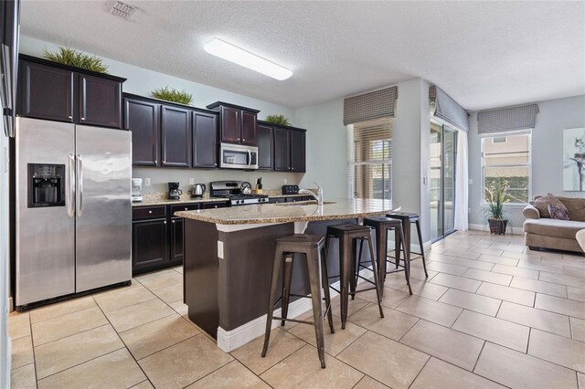 4204 Oakview Dr, Davenport, FL 33837 - kitchen with stainless steel appliances, a breakfast bar, an island with sink, light stone countertops, and a textured ceiling