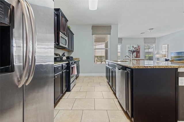 kitchen with stainless steel appliances, a textured ceiling, light tile patterned floors, sink, and a kitchen island with sink