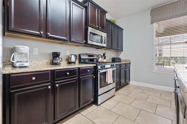 kitchen with stainless steel appliances, light tile patterned flooring, dark brown cabinetry, light stone countertops, and a textured ceiling