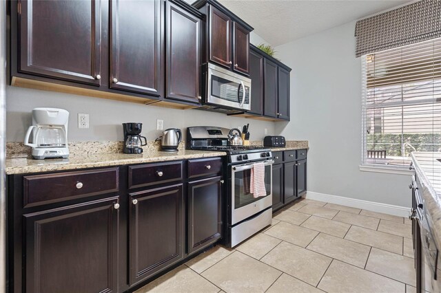 4204 Oakview Dr, Davenport, FL 33837 - kitchen with stainless steel appliances, baseboards, light tile patterned floors, dark brown cabinetry, and light stone countertops