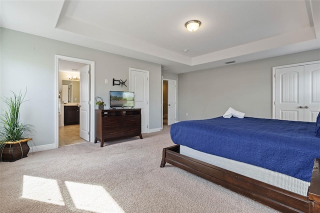 carpeted bedroom featuring ensuite bathroom, a tray ceiling, and a closet