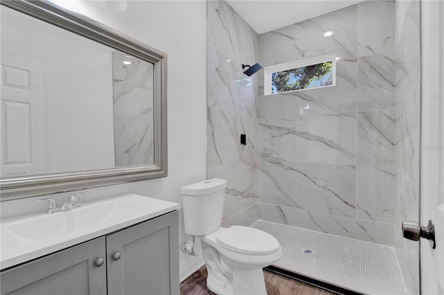 bathroom with hardwood / wood-style flooring, vanity, toilet, and tiled shower