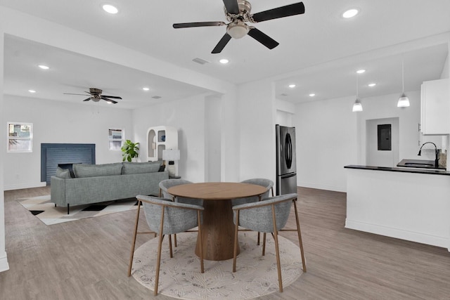 dining area with a brick fireplace, electric panel, wood-type flooring, sink, and ceiling fan