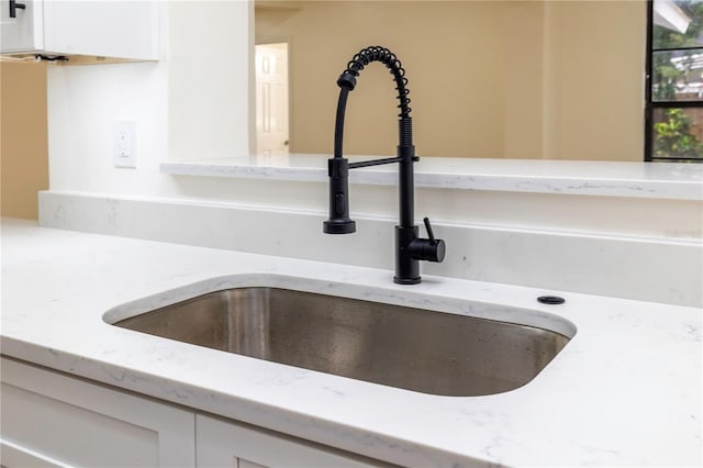 interior details with white cabinets, sink, and light stone counters