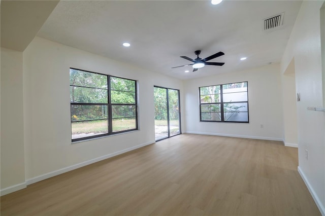 empty room with ceiling fan, plenty of natural light, and light hardwood / wood-style flooring