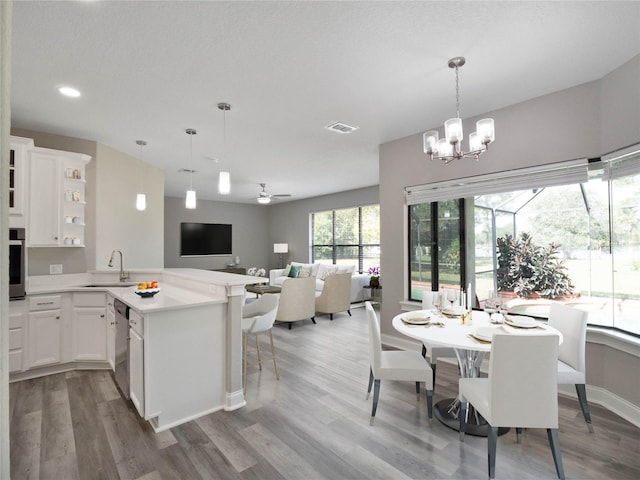 kitchen featuring pendant lighting, kitchen peninsula, sink, hardwood / wood-style flooring, and white cabinetry