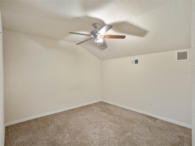 empty room with carpet flooring, a textured ceiling, ceiling fan, and vaulted ceiling